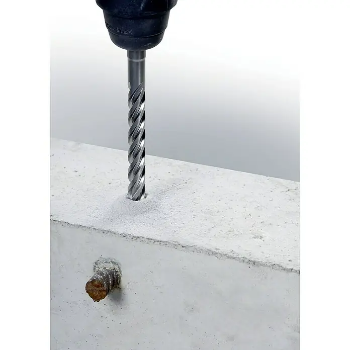 Alpen Beton- & Steinbohrer F8 - 1 Stk., Durchmesser Bohrer: 16 mm, Länge: 260 mm - Eine Nahaufnahme eines Bohrers, der in einen Betonblock bohrt und auf eine Armierung stößt, wobei der Fokus auf dem Bohrer und dem Beton liegt.