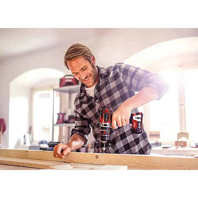 Einhell Professional Power X-Change 18V Akku-Schlagbohrschrauber TP-CD 18/50 Li-i BL - 18 V, 2 Akkus, 2 Ah - 4 Ah, 50 Nm - Ein Mann benutzt einen Einhell Akku-Bohrschrauber, um ein Holzbrett zu bearbeiten. Er trägt ein kariertes Hemd und lächelt.