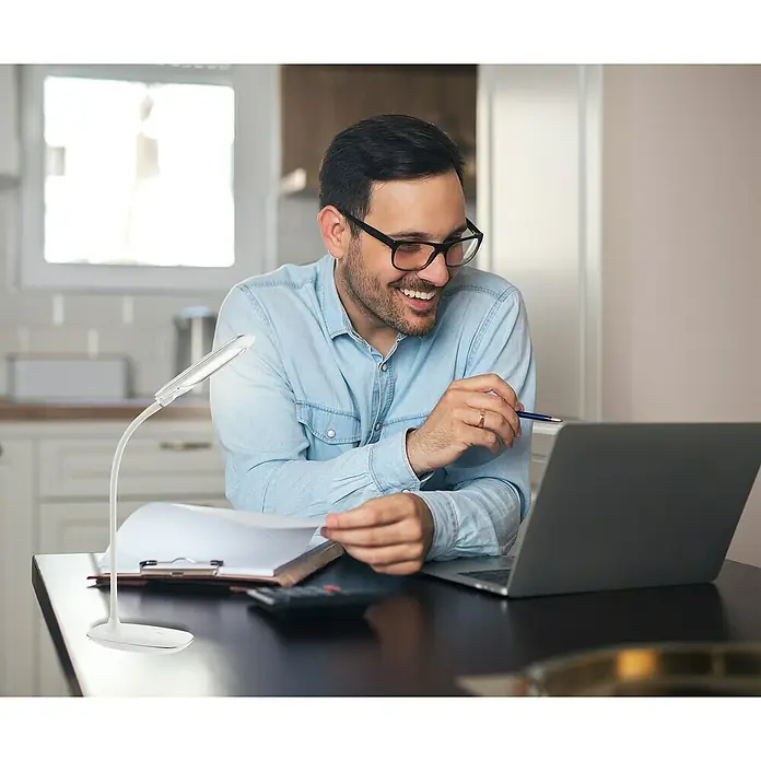 Globo LED-Tischleuchte Minea I - 5 W, L x B x H: 29 x 9,3 x 56 cm, Weiß, Chrom, Transparent, Tageslichtweiß - Ein Mann mit Brille arbeitet am Laptop. Eine moderne Schreibtischlampe sorgt für optimales Licht beim Arbeiten im Homeoffice.