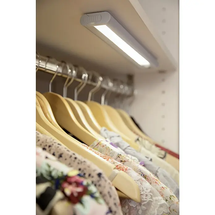 Ledvance LED-Unterbauleuchte - 1,4 W, Kaltweiß, Länge: 300 mm, Betriebsart: Batteriebetrieben - Eine helle LED-Schrankleuchte beleuchtet Kleiderbügel mit floral gemusterten Kleidern in einem Kleiderschrank und sorgt für gute Sicht.