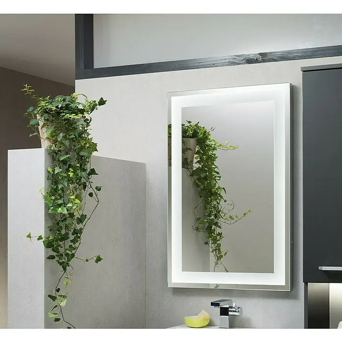 Camargue Stella LED-Lichtspiegel - 80 x 60 cm, Mit eckigen Kanten - Ein beleuchteter Badezimmerspiegel hängt an einer grauen Wand mit einer Pflanze im Spiegelbild, die ein modernes Badezimmerambiente schafft.