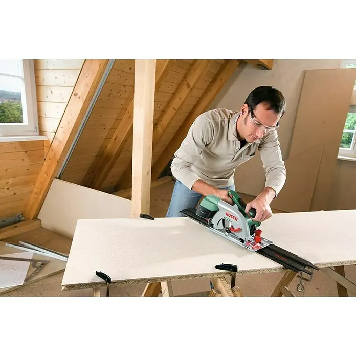 Bosch Handkreissäge PKS 55 A - 1.200 W, 5.600 U/min - Ein Mann benutzt eine Bosch Tauchsäge mit Führungsschiene, um eine Platte zuzuschneiden. Er trägt dabei eine Schutzbrille.