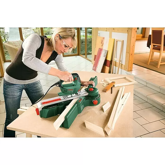 Bosch Elektro-Stichsäge PST 700 E - 500 /min - 3.100 /min, 70 mm, 500 W - Frau sägt mit einer grünen Bosch Stichsäge und Gehrungsführung Holz präzise für einen Rahmen.