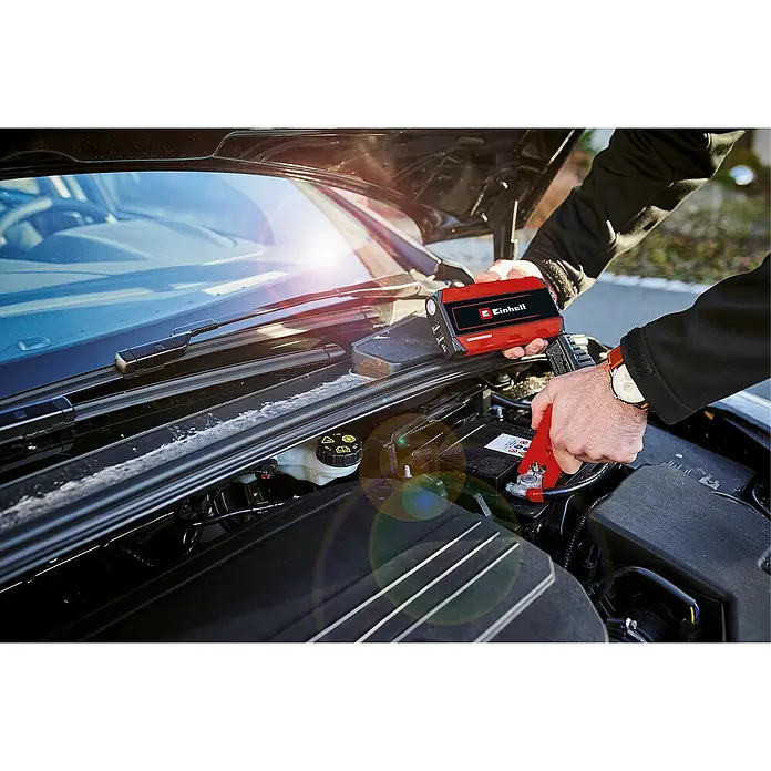 Einhell Kit de arranque CE-JS 12 - 12 V, Corriente máx. de carga: 400 A - Un arrancador de batería Einhell rojo está conectado a una batería de coche para arrancar. Diseño compacto y portátil.