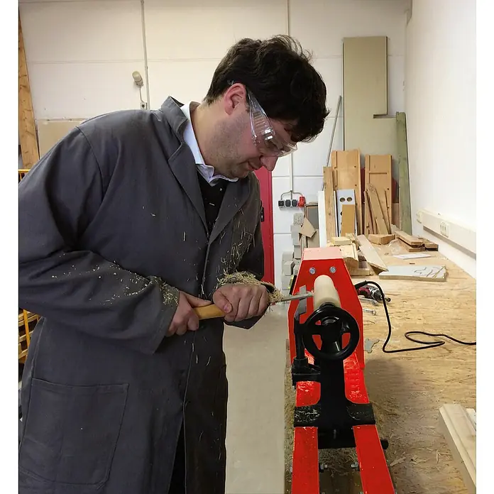 Einhell Torno para madera TC-WW 1000/1 - 890 r.p.m. - 2.600 r.p.m. - Hombre con gafas de seguridad torneando madera en un torno rojo. Virutas de madera están volando.