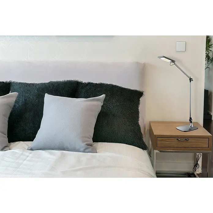 Globo Tischleuchte Pattaya - 10 W, L x B x H: 49 x 17,9 x 96 cm, Grau, Schwarz - Eine moderne LED-Schreibtischlampe auf einem Nachttisch neben einem Bett mit Kissen. Die Lampe ist silberfarben und hat einen verstellbaren Arm.