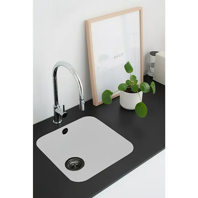 Poalgi Fregadero encastrable Gandía Soft 40 - 44,5 x 44 cm, Material compuesto, Blanco, Brillante - Un moderno fregadero de cocina con un elegante grifo cromado, incrustado en una encimera oscura, junto a una planta verde en maceta y una imagen enmarcada.
