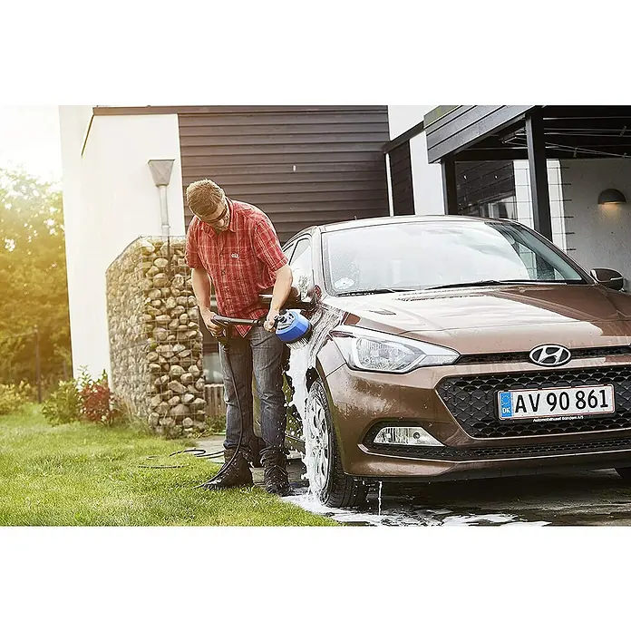 Nilfisk Detergente para automóvil Car Combi Cleaner - 2,5 l - Un hombre lava un coche marrón con un cepillo rotatorio, rodeado de mucha espuma de jabón y con una casa al fondo.