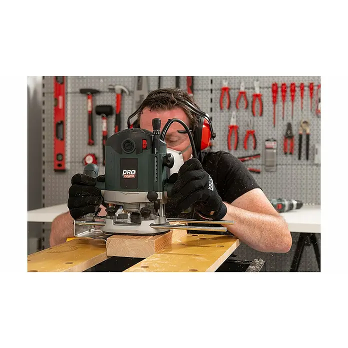 PowerPlus Fresadora eléctrica POWP6050 - 2.100 W, 8.000 r.p.m. - 23.500 r.p.m., Diámetro del portaherramientas: 12 mm - Un hombre usa una fresadora Pro Power para trabajar la madera, usando equipo de seguridad y guantes para trabajar con seguridad.