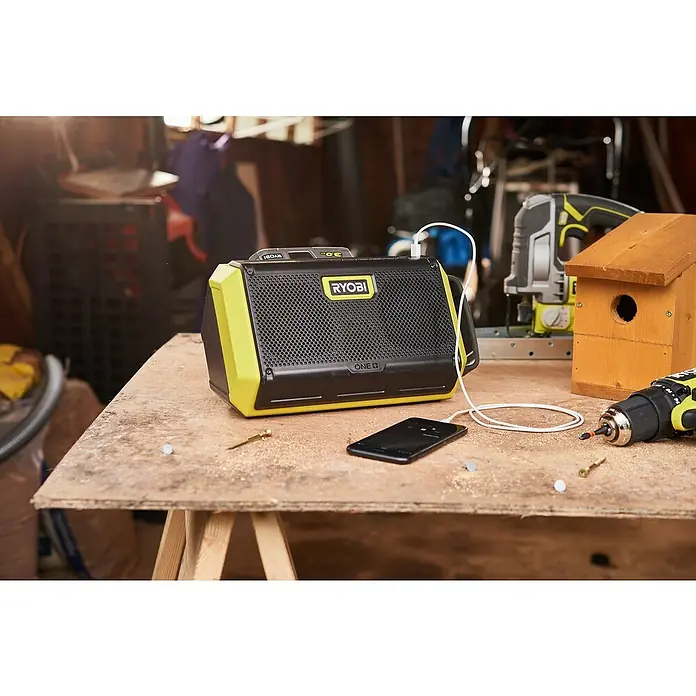 Ryobi ONE+ Altavoz Bluetooth RBT18-0 - 18 V, Sin batería, Potencia de salida altavoz: 15 W - El altavoz Ryobi ONE+ conectado a un smartphone en un banco de trabajo, listo para la música.