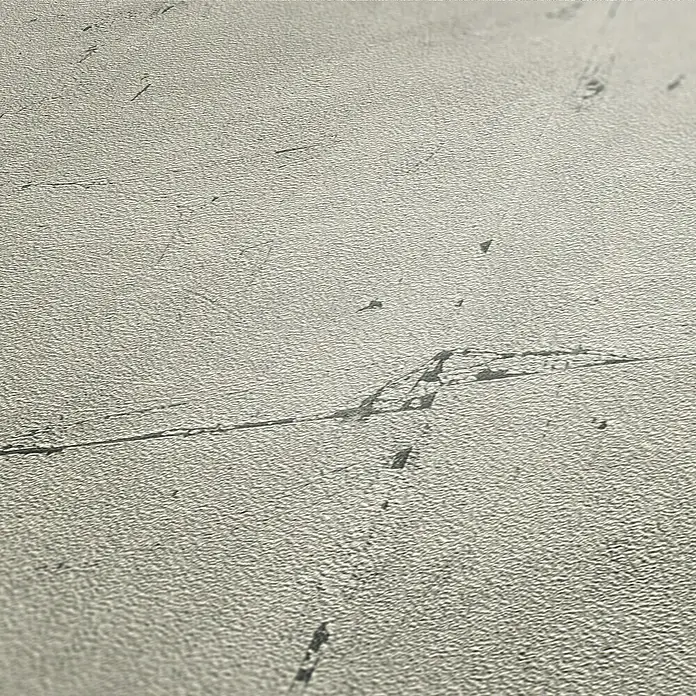 A.S. Création Elements Vliestapete Steinfliese - Grau/Beige, Betonoptik, 10,05 x 0,53 m - Nahaufnahme einer strukturierten, grauen Oberfläche mit dunklen Kratzern und Unregelmäßigkeiten, die eine rustikale Ästhetik erzeugen.