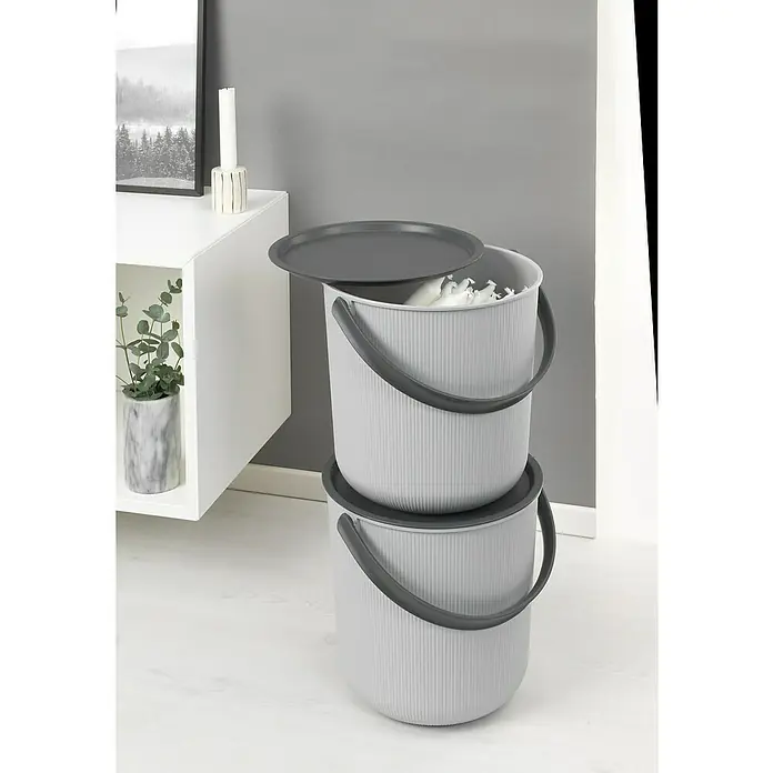 Eimer Akita - L x B x H: 480 x 446 x 445 mm, 53 l, Grau - Zwei graue Eimer mit Deckel übereinander gestapelt, mit dunklen Griffen und Deckeln, neben einem weißen Regal mit Pflanze und Kerze.