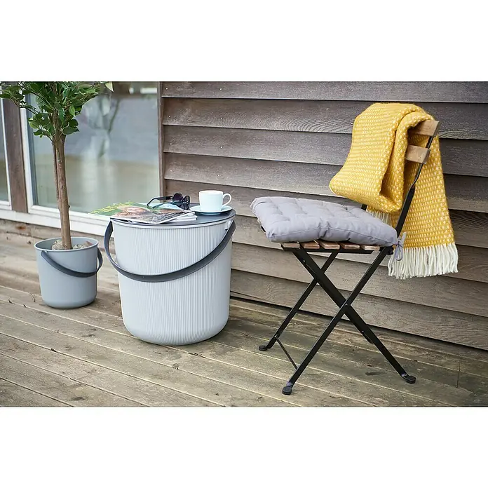 Eimer Akita - L x B x H: 480 x 446 x 445 mm, 53 l, Grau - Outdoor-Szene mit einem grauen Eimer, der als Tisch dient, und einem Klappstuhl mit gelber Decke.