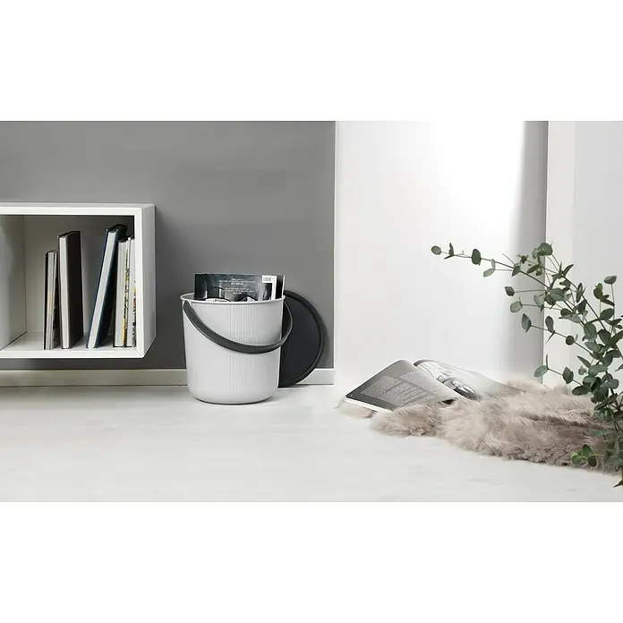 Eimer Akita - L x B x H: 277 x 271 x 258 mm, 10 l, Grau - Ein grauer Eimer mit einem schwarzen Griff und Deckel steht auf einem weißen Boden neben einem Regal mit Büchern.