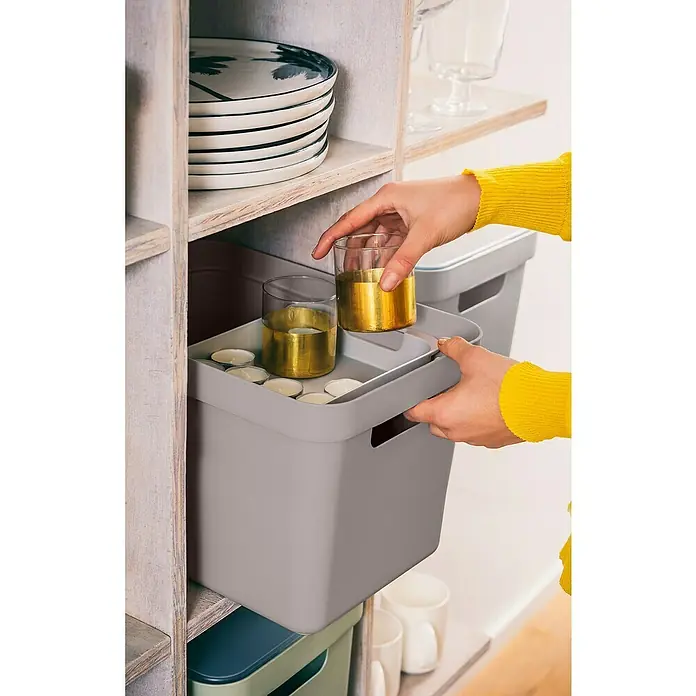 Sunware Aufbewahrungsbox Sigma Home - L x B x H: 35 x 24,6 x 24,3 cm, Kunststoff, Hellgrau - Eine Person ordnet Teelichter und goldene Gläser in einer grauen Aufbewahrungsbox im Regal ein.