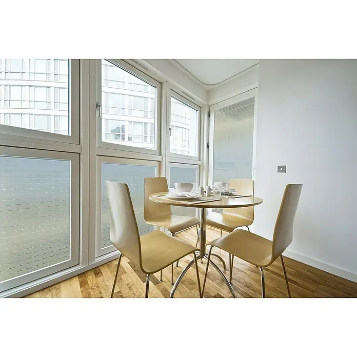 Lámina para ventana Mayo - 45 x 150 cm, Transparente - Comedor luminoso con una mesa redonda y cuatro sillas, puesta con vajilla, junto a grandes ventanas con vistas a un edificio.