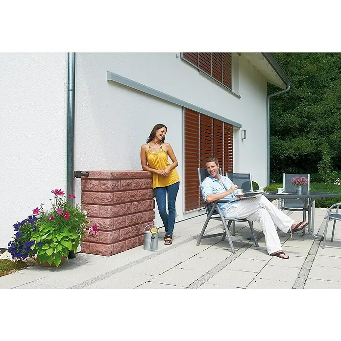 Garantia Exklusive Line Regenspeicher Rocky - 400 l, Redstone - Helle Außenaufnahme eines Hauses mit einer stilvollen Regentonnen in Backsteinoptik und entspannten Menschen im Garten.
