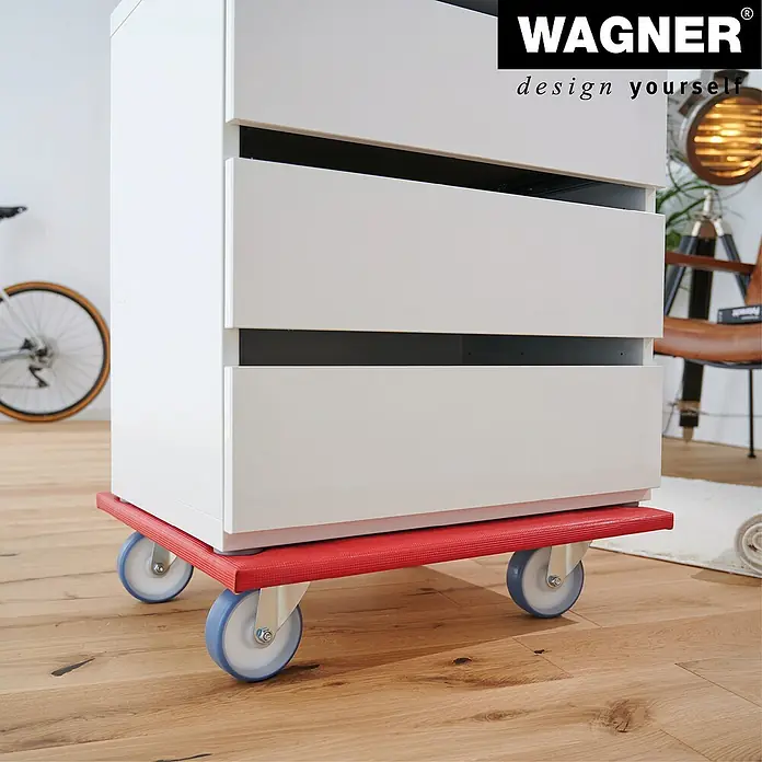Wagner System Transportroller MM1397 - L x B x H: 59 x 49 x 12,3 cm, Traglast: 400 kg, Holz - Das Bild zeigt einen weißen Schrank auf einem roten Möbelroller mit blauen Rädern. Der Möbelroller erleichtert das Verschieben des Schranks.