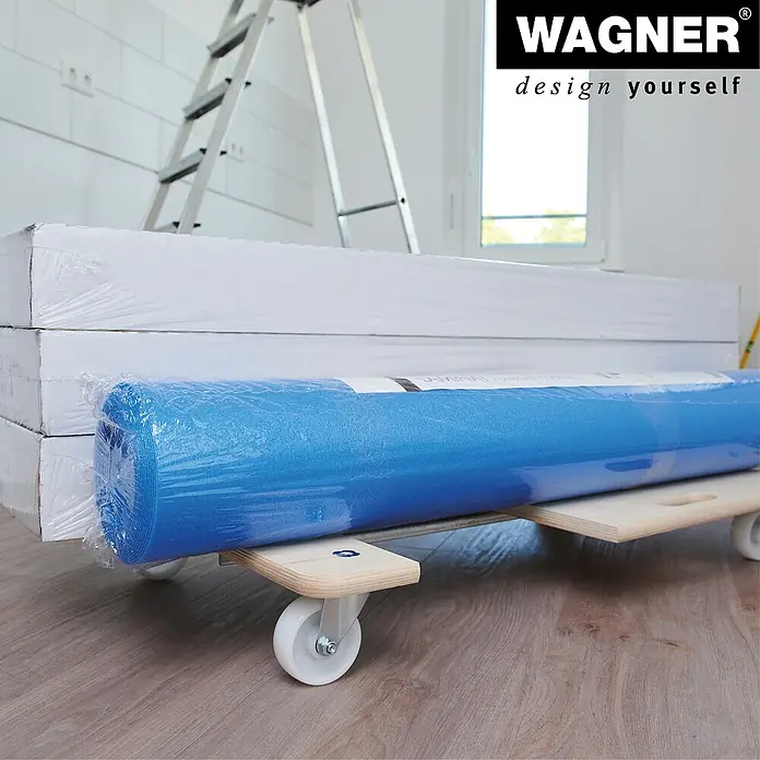Wagner System Transportroller MM 1332 - Traglast: 200 kg, Holz, B x H: 490 x 135 mm - Das Bild zeigt eine Rolle blauen Malervlies auf einem Rollbrett, zusammen mit verpackten Paneelen und einer Leiter im Hintergrund.
