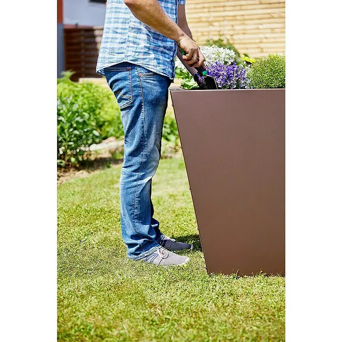 Gutta Hochbeet Valenta 150 - 150 x 90 x 80 cm, Aluminium, Rost Matt - Mann bepflanzt einen hohen, quadratischen Pflanzkübel im Garten mit einer kleinen Schaufel.
