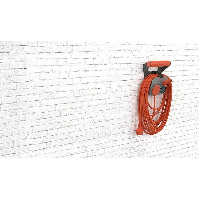 Verlängerungskabel RollON - 10 m, Grau/Rot, IP44, H05VV-F - Das Bild zeigt eine orangefarbene Kabeltrommel an einer weißen Ziegelwand. Die Kabeltrommel ist grau und hat einen Tragegriff.