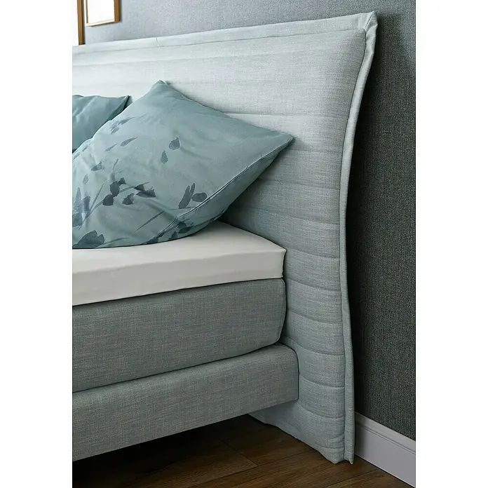 SCHÖNER WOHNEN-Kollektion Vliestapete Unistruktur - Grün/Grau, Uni, 10,05 x 0,53 m - Nahaufnahme eines Boxspringbettes mit hellblauem Kissen und weißem Laken. Der Fokus liegt auf dem Komfort und der hochwertigen Verarbeitung des Bettes.