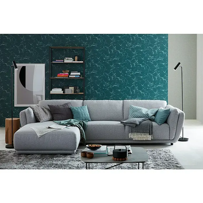 SCHÖNER WOHNEN-Kollektion Vliestapete Marmoroptik - Grün/Grau, Steinoptik, 10,05 x 0,53 m - Modernes Wohnzimmer mit grauem Ecksofa, Bücherregal und abstrakter Kunst. Die Einrichtung wird durch eine Stehlampe und einen Couchtisch ergänzt.