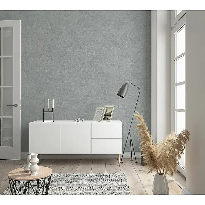 Marburg Sand & Stones Vliestapete Shades - Mittelgrau, Uni, 10,05 x 0,53 m - Ein modernes Wohnzimmer mit einem weißen Sideboard, einer Stehlampe und dekorativen Elementen wie Vasen und Bilderrahmen.