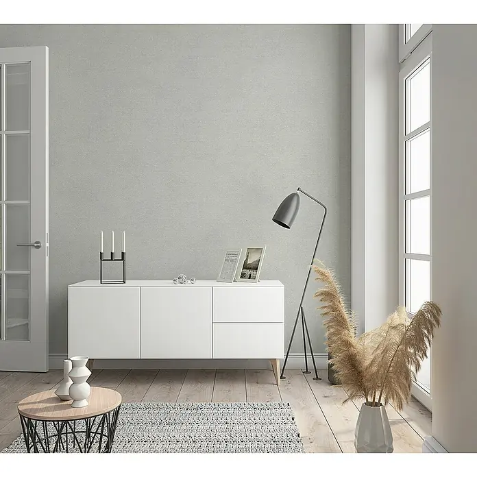 Marburg Sand & Stones Vliestapete Shades - Grau, Uni, 10,05 x 0,53 m - Eine moderne Wohnzimmerszene mit einem weißen Sideboard, einer Stehlampe und dekorativen Elementen.
