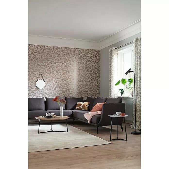 SCHÖNER WOHNEN-Kollektion New Spirit Vliestapete Blüten-Allover - Grau/Gold, Floral, 10,05 x 0,53 m - Ein dunkelgraues Ecksofa aus Stoff in einem Wohnzimmer, mit Kissen und einer Decke, neben einem runden Couchtisch.