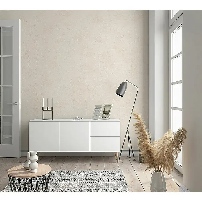 Marburg Sand & Stones Vliestapete Shades - Beigegrau, Uni, 10,05 x 0,53 m - Das Bild zeigt ein modernes Sideboard in Weiß, das mit Dekoartikeln und einer Stehlampe in einem stilvollen Wohnzimmer dekoriert ist.