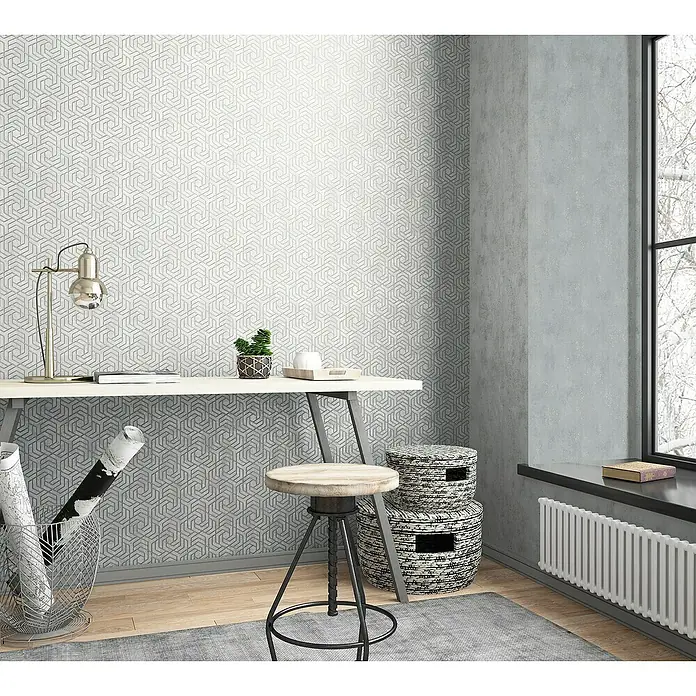 Marburg Sand & Stones Vliestapete City Glam I - Mittelgrau, Betonoptik, 10,05 x 0,53 m - Innenaufnahme eines stilvollen Arbeitsplatzes mit einem Schreibtisch, einer Lampe, einem Hocker und dekorativen Körben vor einer gemusterten Tapete.