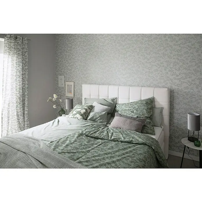 SCHÖNER WOHNEN-Kollektion New Spirit Vliestapete Blüten-Allover - Beige/Blau, Floral, 10,05 x 0,53 m - Schlafzimmer mit Doppelbett, weißem Kopfteil, grüner Bettwäsche mit Blättermuster und passenden Vorhängen.