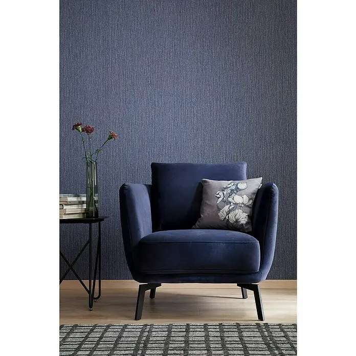 SCHÖNER WOHNEN-Kollektion New Spirit Vliestapete Struktur - Blau, Uni, 10,05 x 0,53 m - Das Bild zeigt einen eleganten marineblauen Sessel mit einem dekorativen Kissen und einem kleinen Beistelltisch mit Blumen in einer Vase.