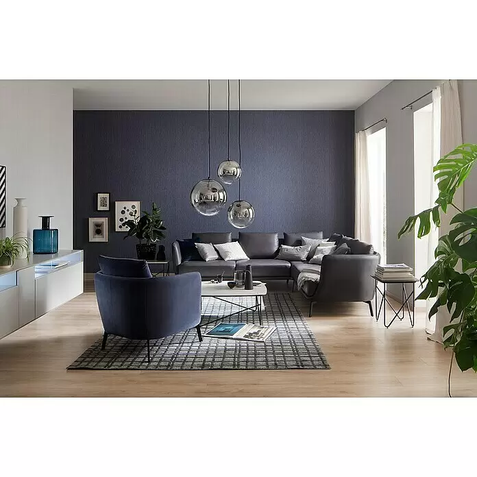SCHÖNER WOHNEN-Kollektion New Spirit Vliestapete Struktur - Blau, Uni, 10,05 x 0,53 m - Modernes Wohnzimmer mit grauem Ecksofa, blauem Sessel, weißem TV-Möbel und stilvollen Pendelleuchten, für eine gemütliche Atmosphäre.
