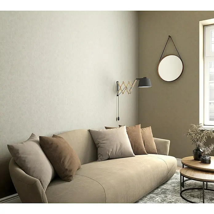 Marburg Sand & Stones Vliestapete Shades - Dunkelbeige, Uni, 10,05 x 0,53 m - Elegantes Wohnzimmer mit beigem Sofa, Zierkissen und einer Wandleuchte. Ein runder Spiegel und Beistelltische ergänzen die stilvolle Einrichtung.
