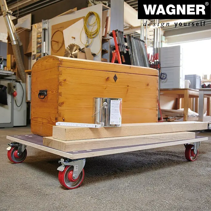 Wagner System Transportroller MM 1349 - L x B x H: 1.200 x 800 x 177 mm, Traglast: 1.000 kg, Holz - Der Wagner Rollbrett mit einer Holzkiste und einer Farbdose darauf, ideal für den Transport schwerer Gegenstände in der Werkstatt.