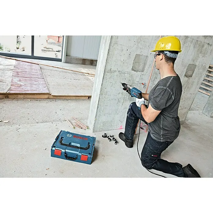 Bosch Professional Martillo combinado GBH 2-28 F - 880 W, 3,2 J, Alojamiento SDS-Plus, Incluye 3 brocas y cinceles - Un trabajador de la construcción con un martillo perforador Bosch en la mano, con una caja de herramientas Bosch a su lado. Herramienta profesional para la construcción.
