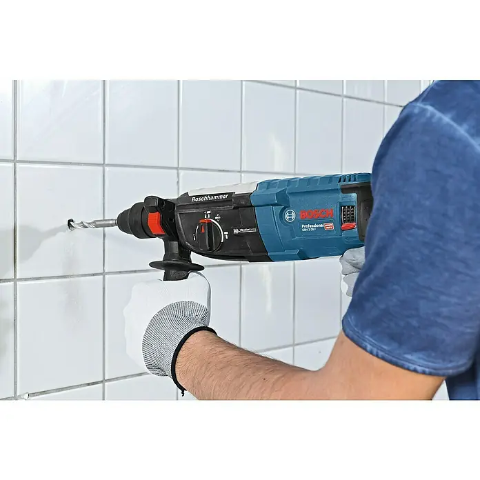 Bosch Professional Martillo combinado GBH 2-28 F - 880 W, 3,2 J, Alojamiento SDS-Plus, Incluye 3 brocas y cinceles - Imagen de un taladro percutor Boschhammer, operado con una mano, perforando agujeros en una pared de azulejos.