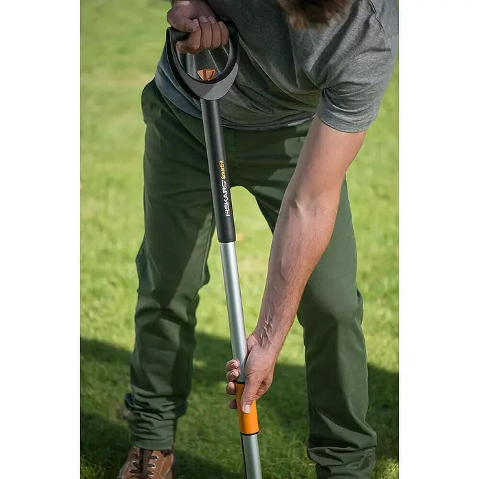 Fiskars Teleskop-Unkrautstecher SmarFit - Länge Stiel: 99 cm - 119 cm - Person, die einen FISKARS SmartFit Spaten hält. Das Werkzeug hat einen verstellbaren Griff für individuelle Anpassung und Komfort bei der Gartenarbeit.