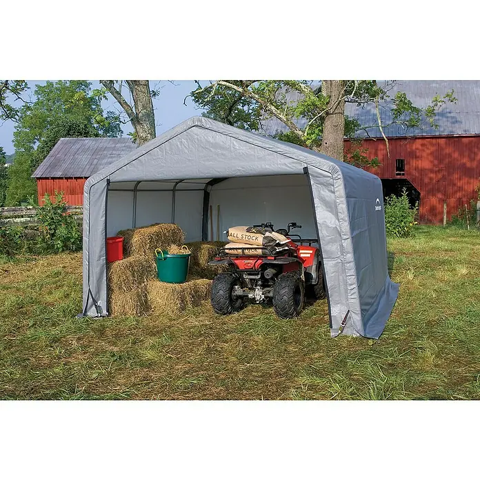 ShelterLogic Gerätehaus - Außenmaß inkl. Dachüberstand (B x T): 370 x 370 cm, Kunststoff, Grau - Das graue ShelterLogic-Carport schützt ein rotes ATV, Heuballen und eine grüne Wanne. Es steht auf einer grünen Wiese vor einer roten Scheune.