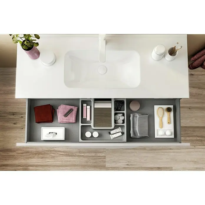Riva Urban Einbauwaschbecken - 60,8 x 46 cm, Weiß - Ein Waschbeckenschrank mit offenem Schubfach, das eine graue Ablage mit Kosmetikartikeln und Accessoires zeigt.