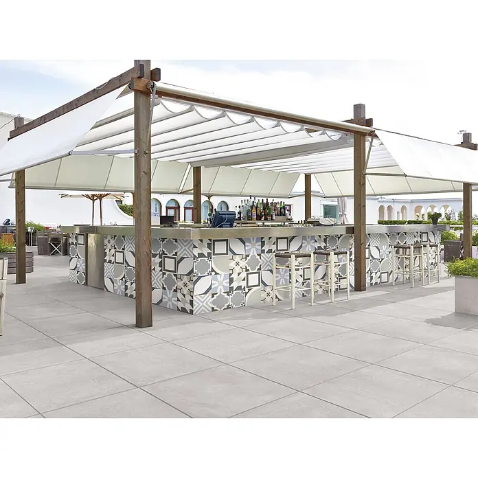Terrassenfliese Click and Go Square Concrete - 60 x 60 cm, Grau, Matt - Eine Außenbar mit bunten Fliesen unter einer Pergola. Die Bar verfügt über Barhocker und eine Auswahl an Getränken.