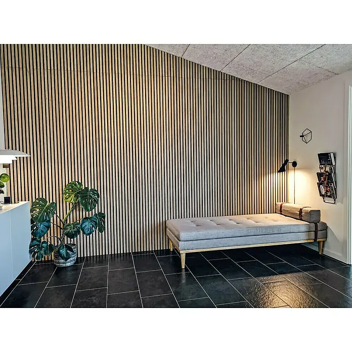 FibroTech Akustikpaneel Premium - Light Oak, 2.440 x 605 x 22 mm - Einrichtungsidee mit Holzpaneelen an der Wand, einem stilvollen Sofa und einer Zimmerpflanze, die eine gemütliche Atmosphäre schafft.