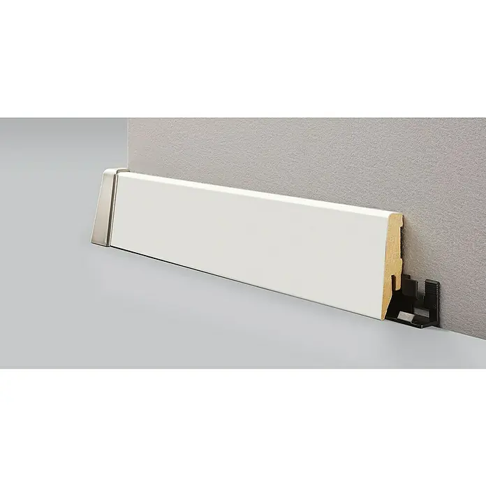 LOGOCLIC Sockelleiste K58 Weiß Matt - 260 cm x 18 mm x 58 mm, MDF/HDF - Detailansicht einer weißen Sockelleiste mit Metallecke und Montageclips. Die Leiste ist an einer grauen Wand befestigt.