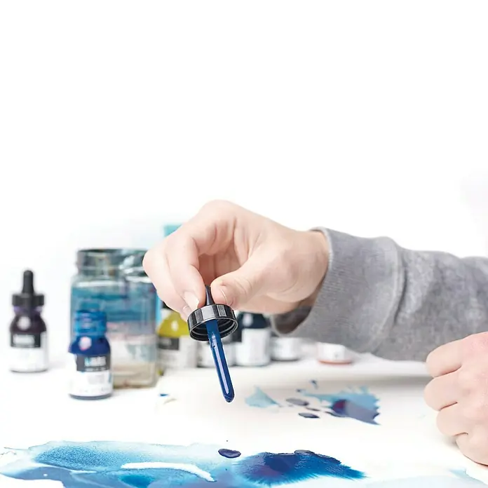 Liquitex Professional Zeichentinte - Titanweiß, 30 ml, Flasche mit Tropfpipette - Nahaufnahme von blauer Tinte, die aus einer Pipette tropft, um lebendige Kunst zu schaffen. Der Fokus liegt auf der Intensität der Farbe und ihrer fließenden Bewegung.