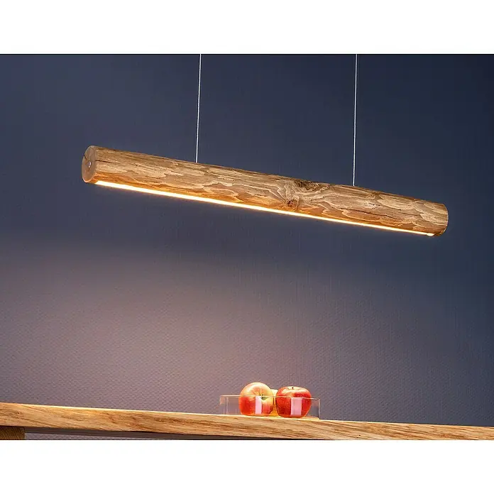 Spotlight LED-Pendelleuchte Lucas - 25,5 W, Braun/Gebeizte Kiefer, 90 cm - Eine moderne, hölzerne Hängelampe in Form eines Baumstamms, die warmes Licht abgibt, hängt über einem Holztisch mit Äpfeln.