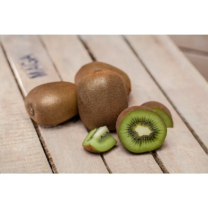 Piardino Kiwi - Actinidia chinensis, Tamaño de maceta: 15 cm - Primer plano de kiwis frescos sobre una superficie de madera, algunos enteros, otros cortados para mostrar la pulpa verde.
