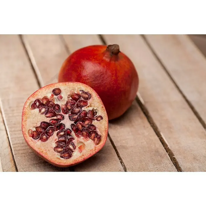 Granado - Punica granatum - Una granada cortada y una granada entera se encuentran sobre una mesa de madera, revelando las semillas rojas de la granada cortada.