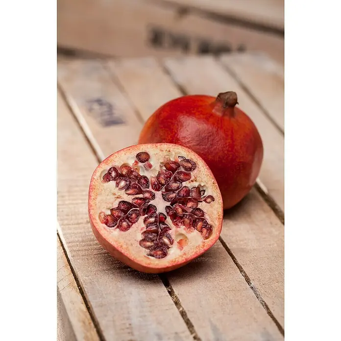 Granado - Punica granatum - Primer plano de una granada cortada y una granada entera sobre una mesa rústica de madera.